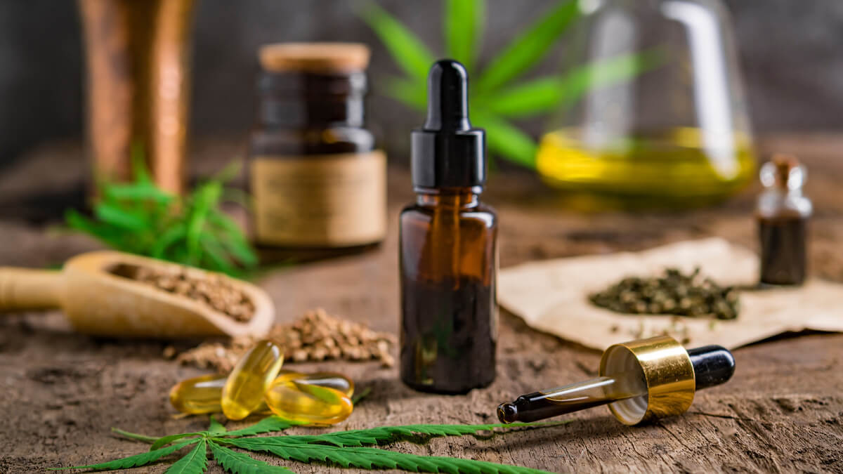 Bočica CBD ulja, kapsule i listovi konoplje na drvenom stolu – prirodan izvor za podršku tijelu i umu.